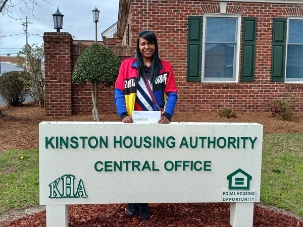 Woman standing behind the Kinston Housing Authority Sign.