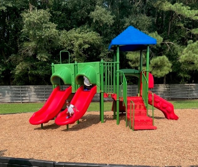 A playground slide set with a girl going down one of the slides.