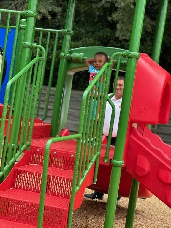 A little boy standing on the platform of a slide.