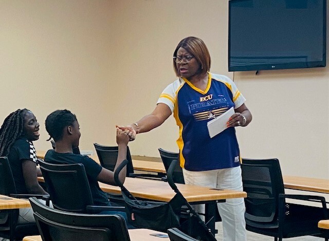 A woman giving a fist bump to one of the two young adults.