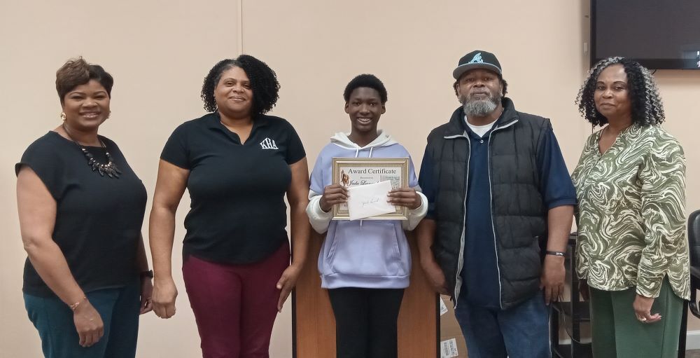 Jada Leonard holding an award surrounded by family and HA employees. 