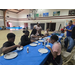  Six people sit around a table, while two people stand and supervise. 