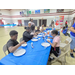  Six people sit around a table making slime with one person supervising. 