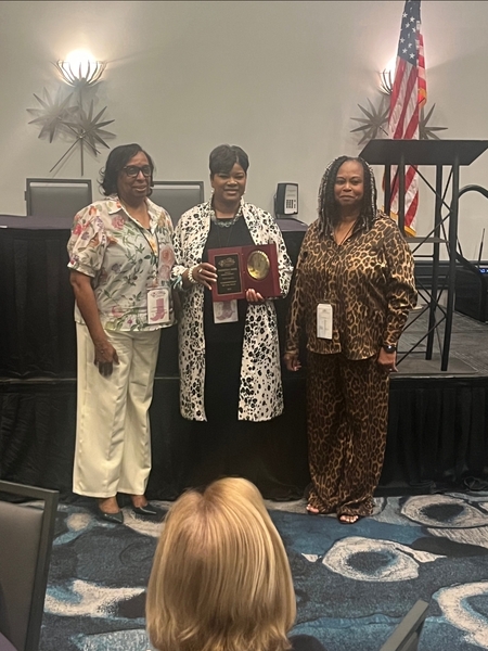 Three women smile for a picture holding an award